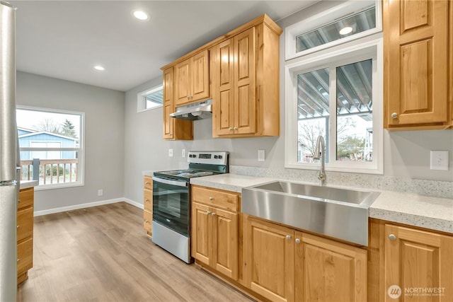 kitchen with a sink, under cabinet range hood, light wood finished floors, stainless steel electric range oven, and baseboards