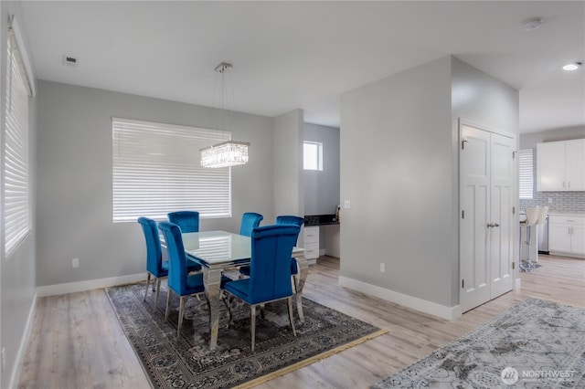 dining area with light wood finished floors, a notable chandelier, and baseboards