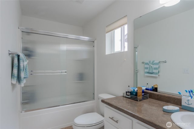 bathroom with combined bath / shower with glass door, toilet, and vanity