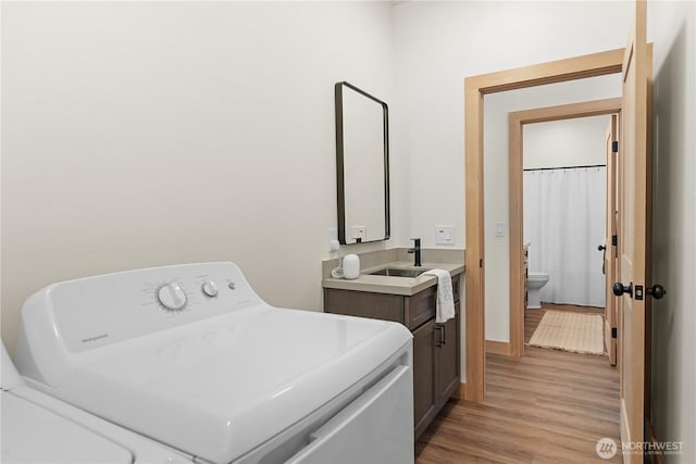 washroom featuring light wood finished floors, baseboards, cabinet space, washer / clothes dryer, and a sink