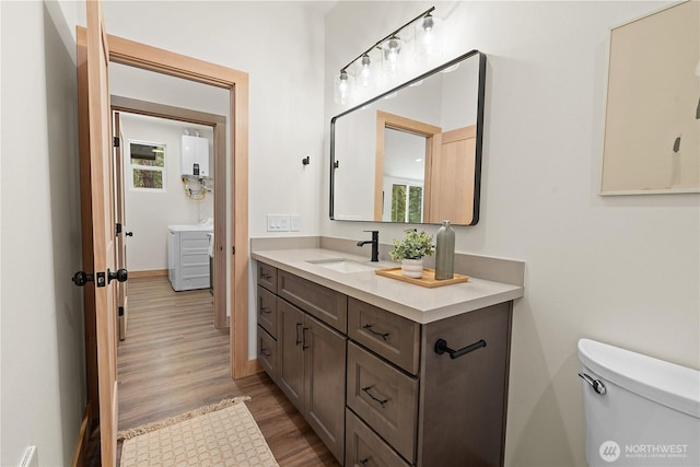 bathroom featuring vanity, wood finished floors, tankless water heater, a healthy amount of sunlight, and toilet