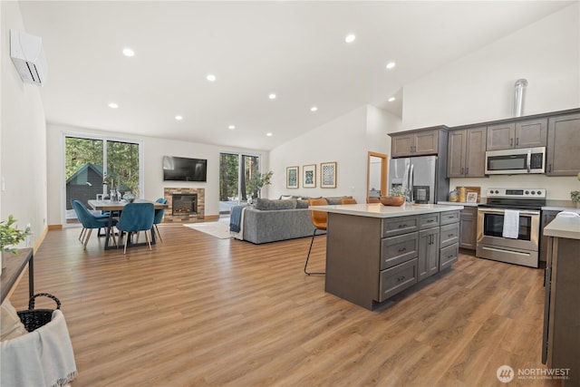 kitchen with light countertops, an AC wall unit, appliances with stainless steel finishes, a kitchen bar, and open floor plan