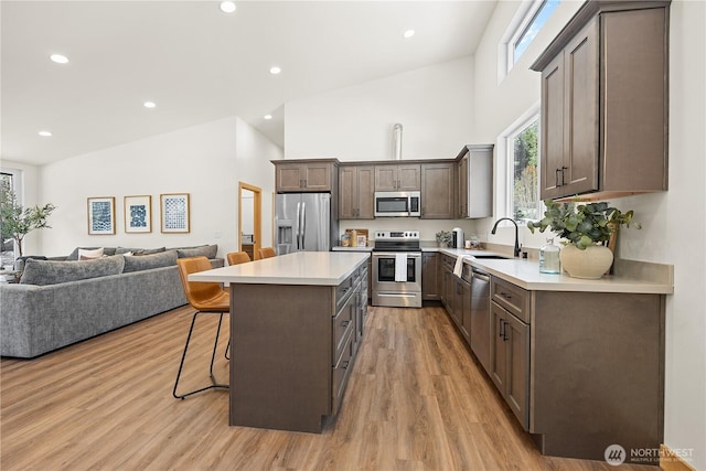 kitchen featuring open floor plan, a breakfast bar, light wood-style floors, stainless steel appliances, and a sink