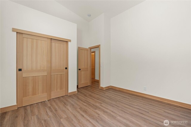 unfurnished bedroom with a closet, baseboards, high vaulted ceiling, and wood finished floors