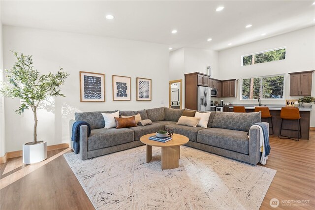 living area with a high ceiling, recessed lighting, and light wood-style floors