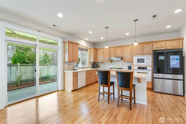 kitchen with light brown cabinetry, under cabinet range hood, light wood-type flooring, light countertops, and white appliances