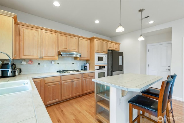 kitchen with a kitchen island, under cabinet range hood, light wood-type flooring, decorative backsplash, and white appliances