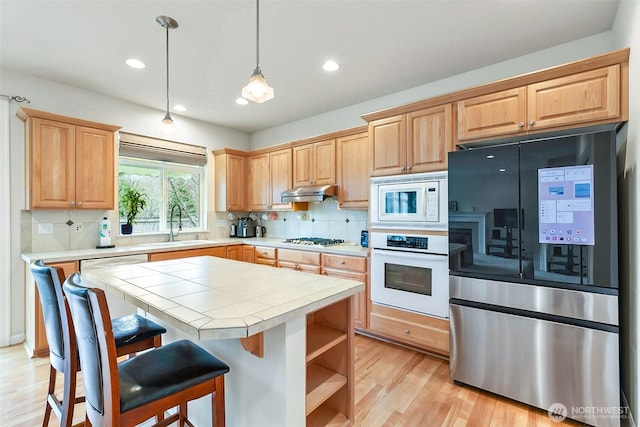 kitchen with light brown cabinets, under cabinet range hood, a sink, white appliances, and tile counters