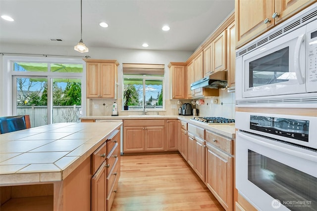 kitchen with light brown cabinetry, under cabinet range hood, a sink, white appliances, and tile counters