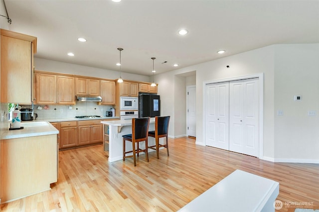 kitchen featuring under cabinet range hood, white appliances, a breakfast bar, and light countertops