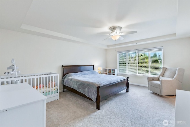 bedroom featuring light carpet, baseboards, a ceiling fan, and a tray ceiling