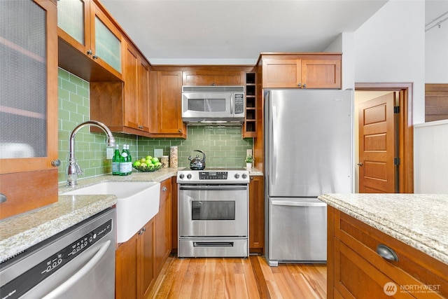 kitchen featuring tasteful backsplash, light wood-style flooring, appliances with stainless steel finishes, brown cabinetry, and a sink