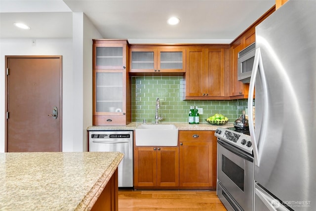 kitchen with light wood-style flooring, a sink, light countertops, appliances with stainless steel finishes, and tasteful backsplash