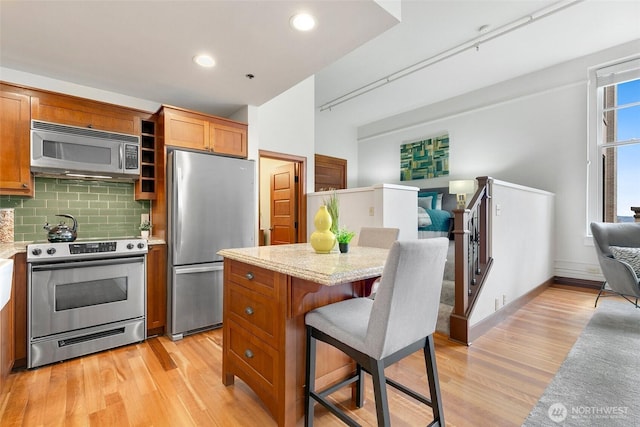 kitchen featuring light wood-type flooring, backsplash, appliances with stainless steel finishes, and open floor plan