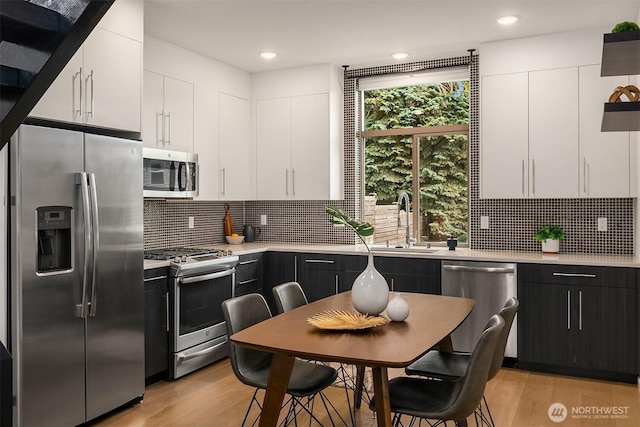 kitchen with light wood-style flooring, a sink, light countertops, appliances with stainless steel finishes, and white cabinetry