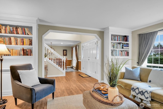 living room featuring built in features, baseboards, ornamental molding, stairs, and light wood-type flooring