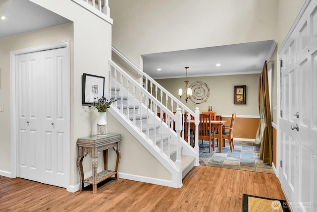 stairway with wood finished floors, recessed lighting, crown molding, baseboards, and a chandelier