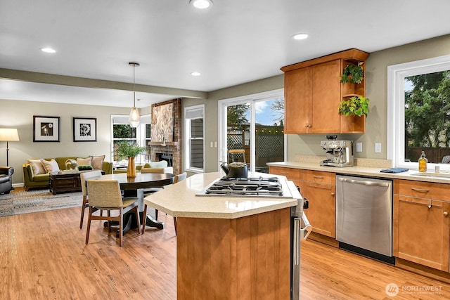 kitchen featuring light wood-style flooring, open floor plan, a stone fireplace, appliances with stainless steel finishes, and light countertops