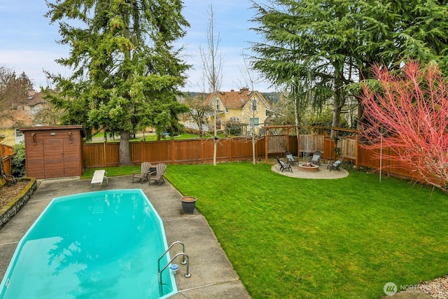 view of swimming pool featuring an outbuilding, a fenced backyard, a shed, an outdoor fire pit, and a yard