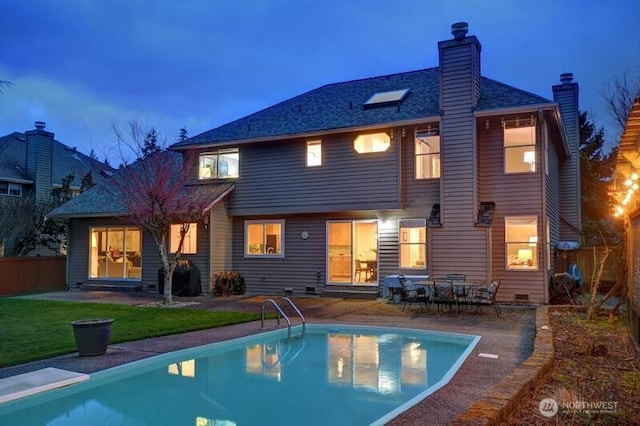 back of house at dusk with fence, a lawn, a chimney, a patio area, and an outdoor pool