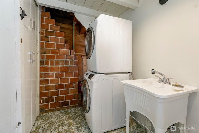 laundry area with a sink, brick wall, laundry area, and stacked washer / dryer