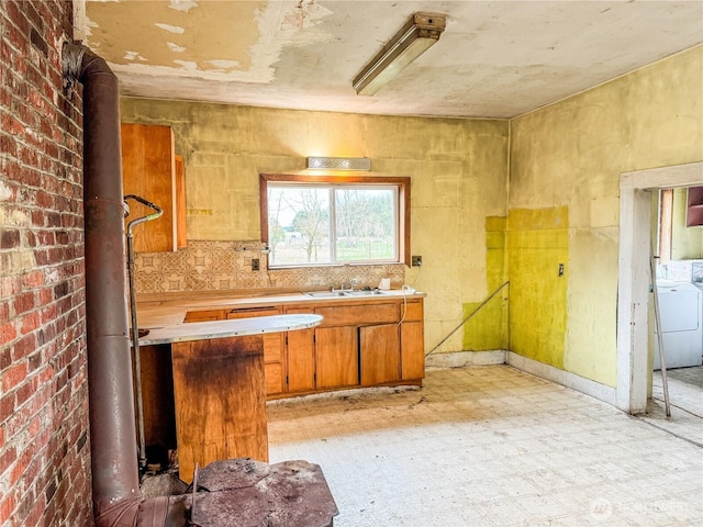 kitchen featuring light floors, light countertops, washer / dryer, brown cabinetry, and a sink