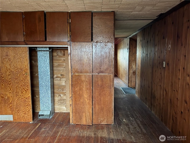 hall featuring dark wood-type flooring, visible vents, and wood walls