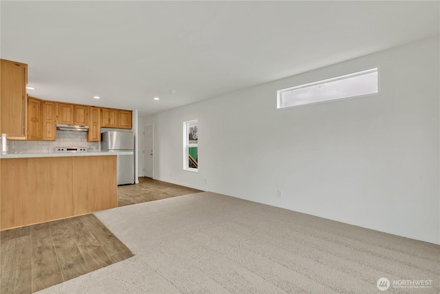 kitchen with backsplash, under cabinet range hood, light countertops, recessed lighting, and freestanding refrigerator