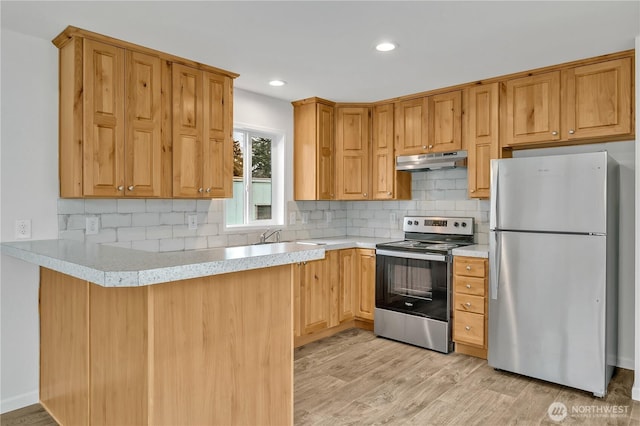 kitchen featuring tasteful backsplash, under cabinet range hood, light countertops, light wood-style flooring, and appliances with stainless steel finishes