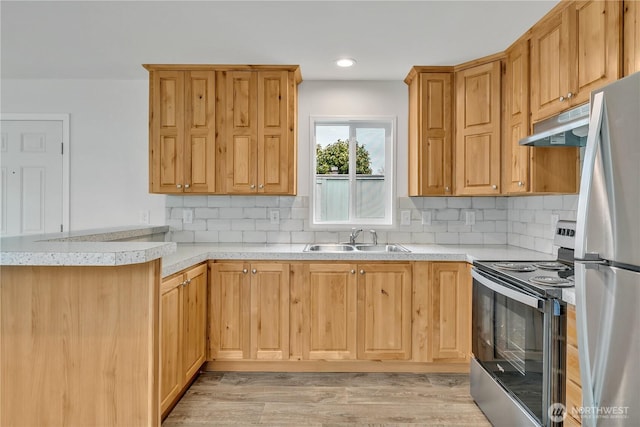 kitchen featuring a peninsula, a sink, light countertops, under cabinet range hood, and appliances with stainless steel finishes