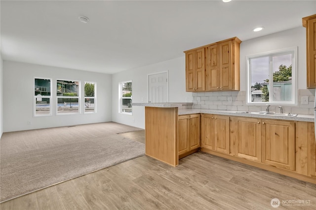 kitchen with light wood finished floors, backsplash, open floor plan, light countertops, and a peninsula