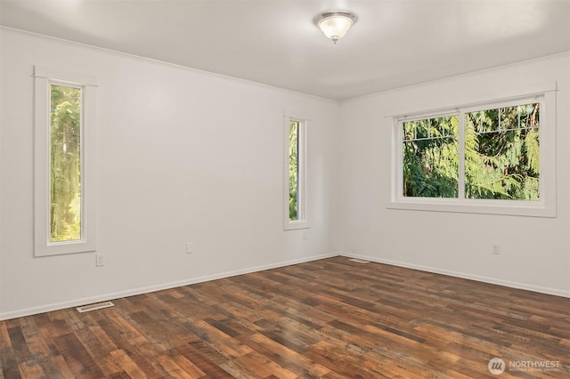 spare room featuring visible vents, crown molding, baseboards, and dark wood-style flooring