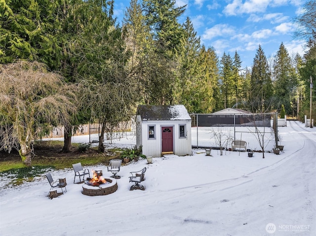 snowy yard with an outdoor structure, fence, a storage shed, and an outdoor fire pit