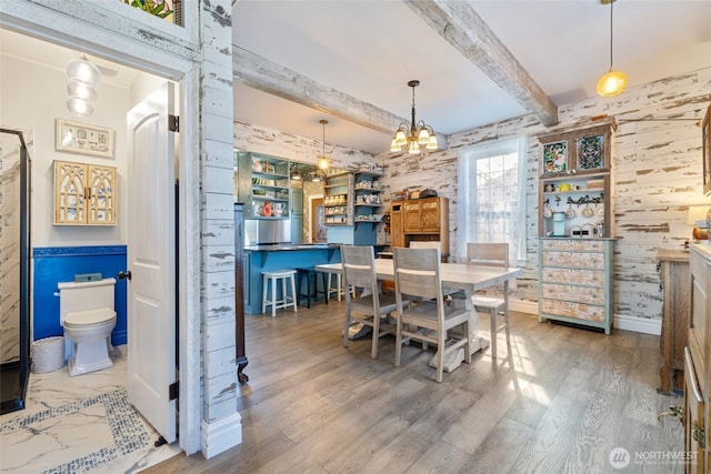 dining area with beamed ceiling, wooden walls, an inviting chandelier, and wood finished floors