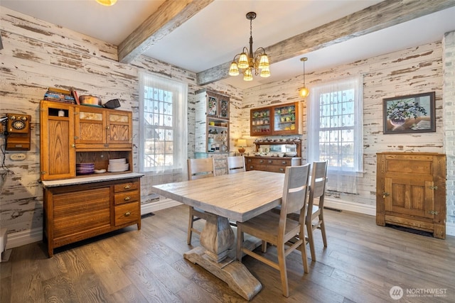 dining area featuring beam ceiling, a chandelier, baseboards, and wood finished floors