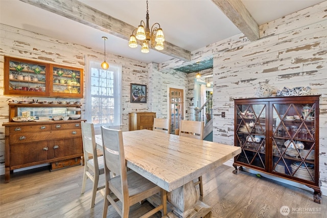 dining area featuring beam ceiling, a notable chandelier, and light wood finished floors