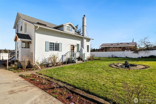 rear view of property with a lawn, a chimney, and fence