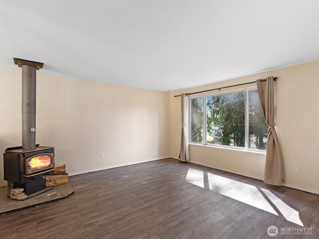unfurnished living room featuring a wood stove, wood finished floors, and baseboards