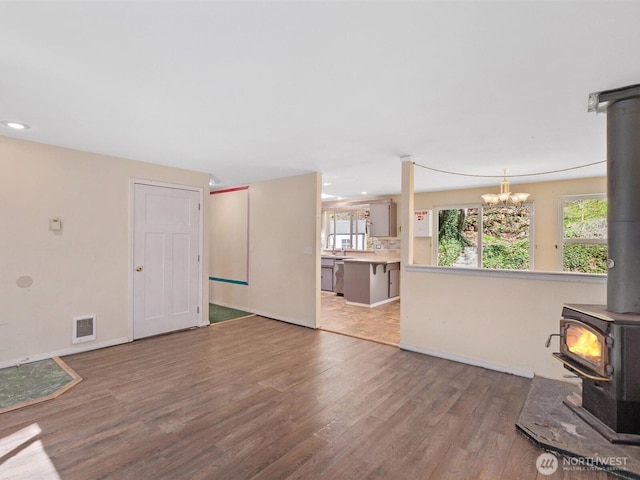 unfurnished living room with visible vents, baseboards, a wood stove, a chandelier, and wood finished floors
