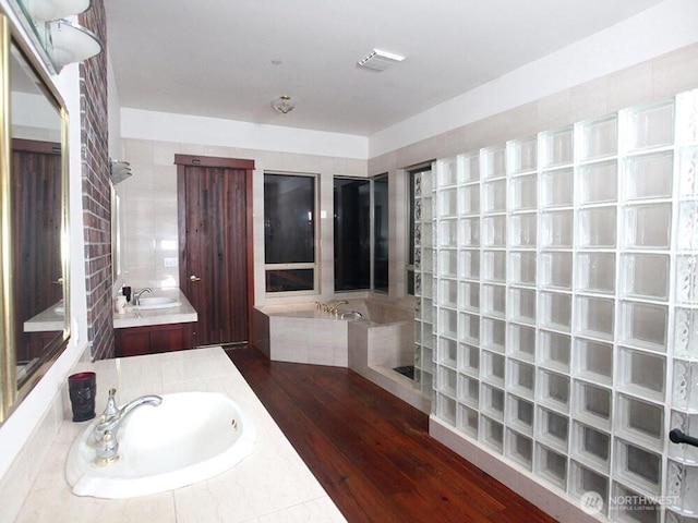 bathroom featuring vanity, a bath, wood finished floors, and a tile shower