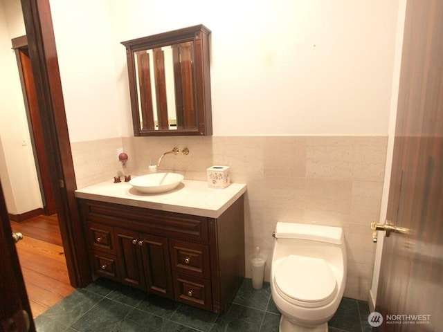 half bathroom with tile patterned floors, toilet, tile walls, and vanity