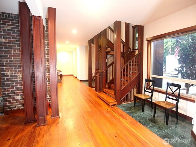 corridor with stairs, baseboards, hardwood / wood-style floors, and brick wall