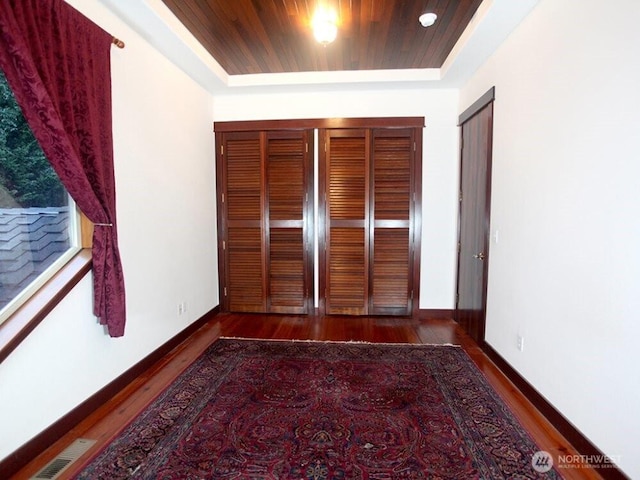 unfurnished bedroom with wood finished floors, baseboards, visible vents, wood ceiling, and a raised ceiling