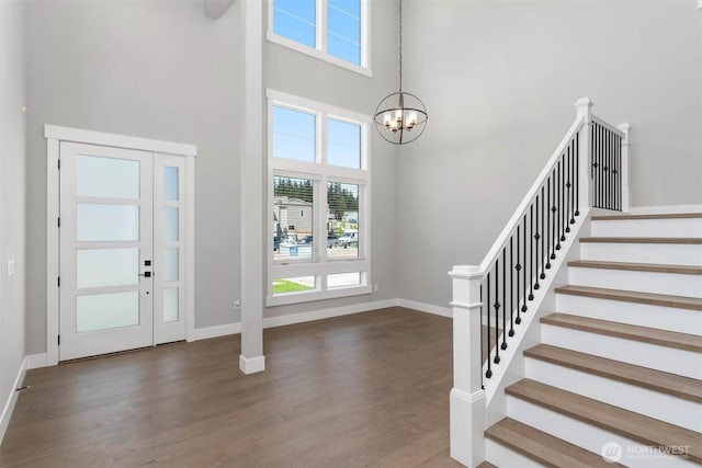 entryway with wood finished floors, a high ceiling, baseboards, a chandelier, and stairs