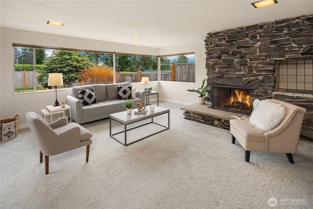 living area with baseboards, a stone fireplace, and carpet flooring