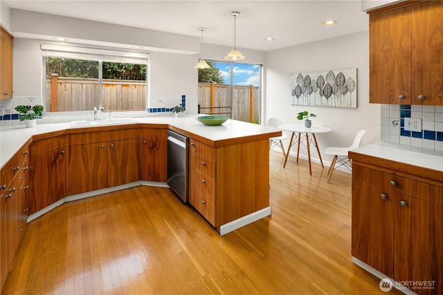 kitchen with a peninsula, a sink, light countertops, stainless steel dishwasher, and light wood-type flooring