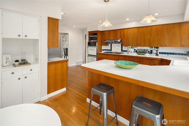 kitchen featuring brown cabinetry, light wood finished floors, appliances with stainless steel finishes, and under cabinet range hood