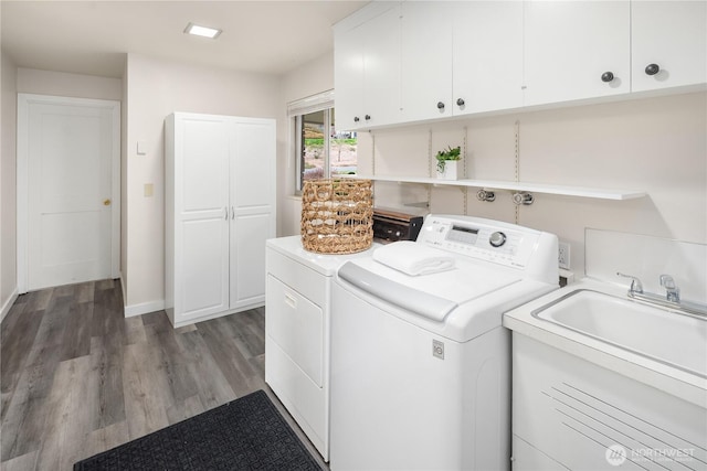 clothes washing area featuring a sink, wood finished floors, washing machine and dryer, cabinet space, and baseboards