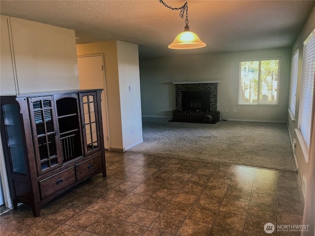 unfurnished living room with baseboards, a textured ceiling, a fireplace, and dark carpet