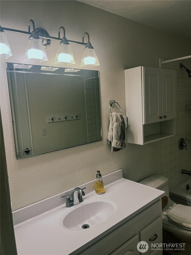 bathroom featuring vanity,  shower combination, toilet, and a textured wall